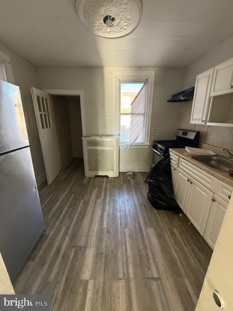 kitchen featuring stainless steel refrigerator, white cabinetry, sink, and ventilation hood