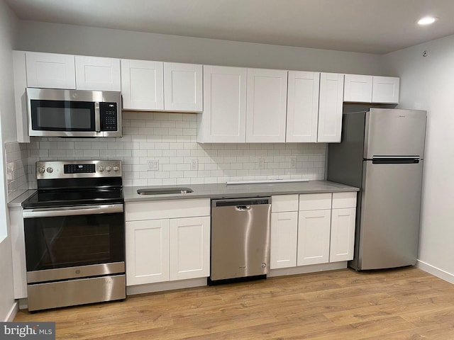 kitchen with decorative backsplash, stainless steel appliances, white cabinetry, and light hardwood / wood-style flooring