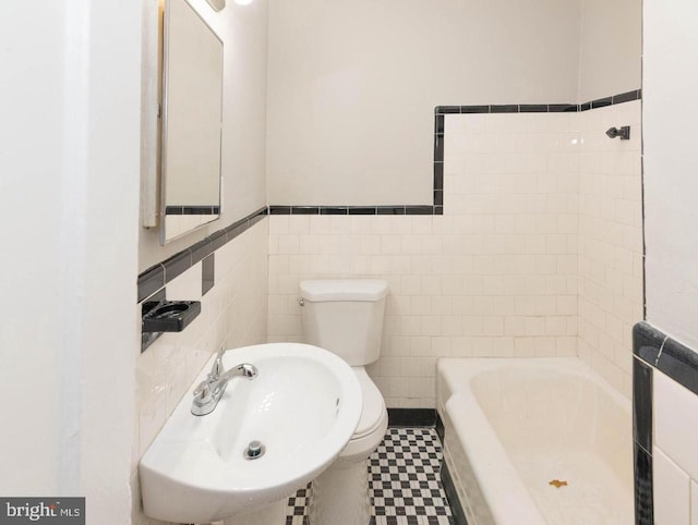 bathroom featuring a washtub, toilet, tile walls, and sink