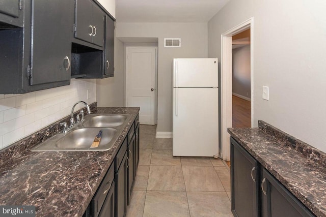 kitchen featuring sink, tasteful backsplash, white refrigerator, dark stone counters, and light tile patterned floors