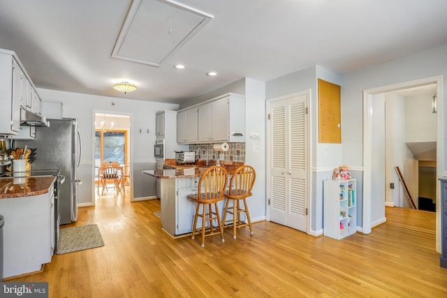 kitchen featuring a breakfast bar area, kitchen peninsula, light hardwood / wood-style flooring, and white cabinets