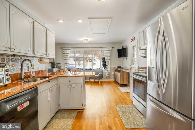 kitchen featuring kitchen peninsula, appliances with stainless steel finishes, sink, light hardwood / wood-style flooring, and white cabinets