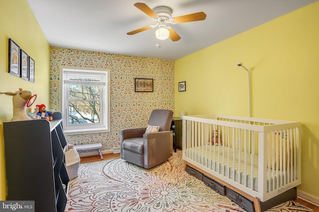 bedroom with hardwood / wood-style flooring, ceiling fan, and a nursery area