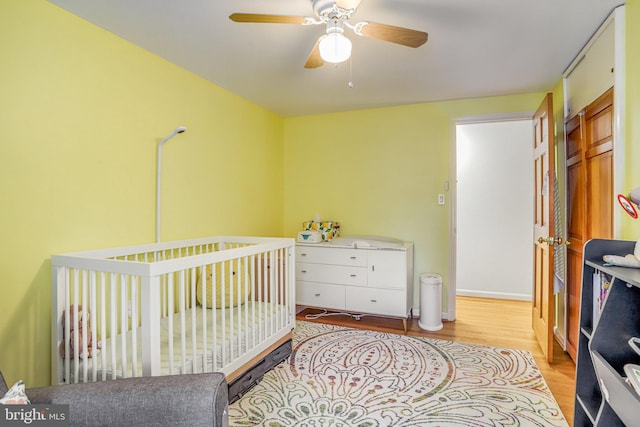 bedroom with ceiling fan, light hardwood / wood-style floors, a crib, and a closet