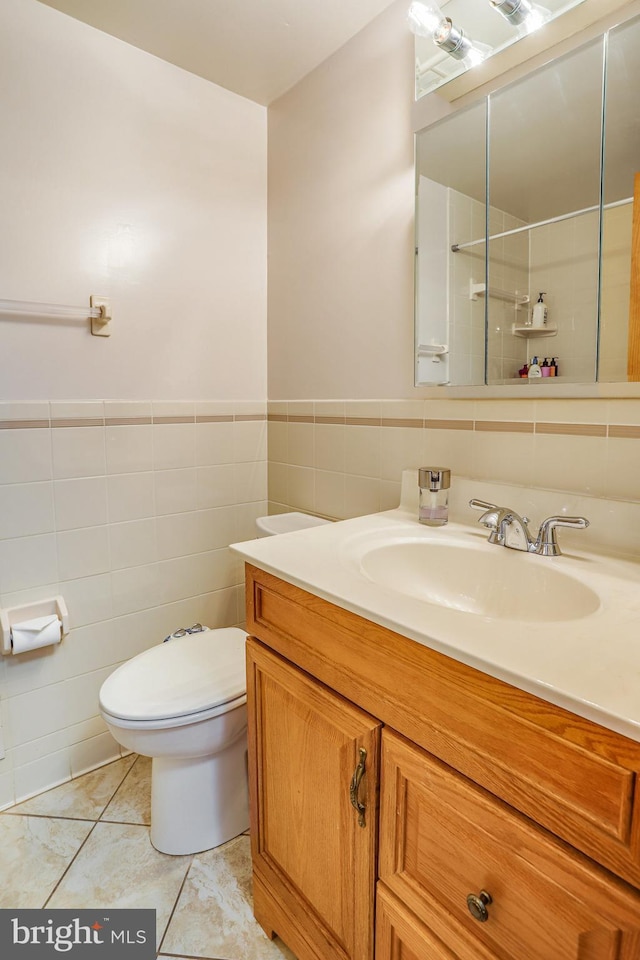 bathroom featuring toilet, vanity, tile patterned floors, and tile walls