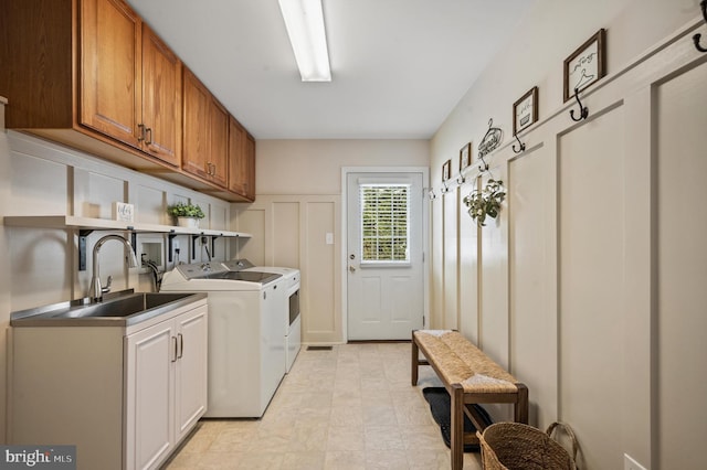 clothes washing area featuring cabinets, sink, and washer and clothes dryer