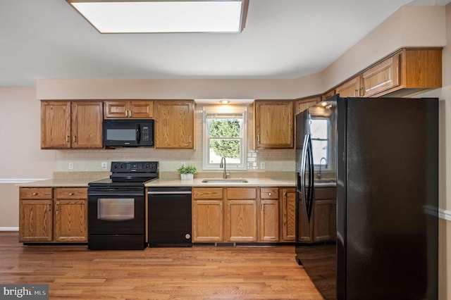 kitchen with tasteful backsplash, light hardwood / wood-style floors, sink, and black appliances