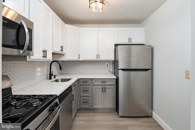 kitchen featuring white cabinetry, stainless steel appliances, sink, gray cabinets, and light wood-type flooring