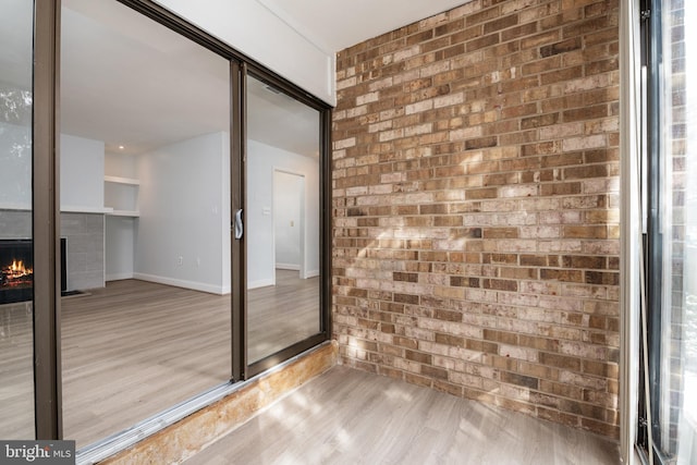 empty room with brick wall, a multi sided fireplace, and light hardwood / wood-style floors