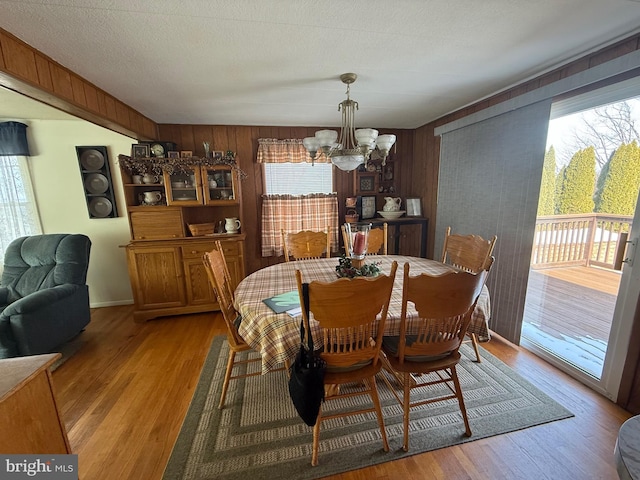 dining area with wooden walls, light hardwood / wood-style flooring, and a notable chandelier