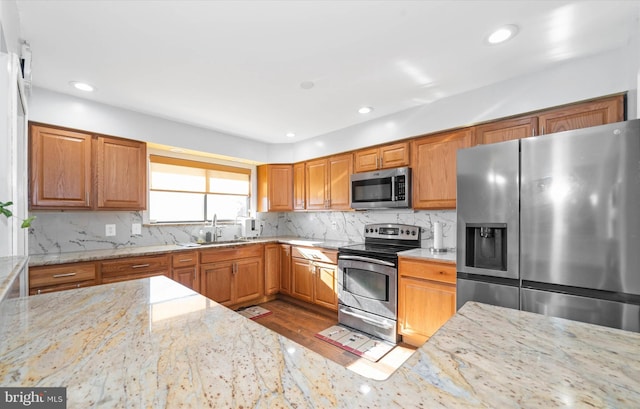 kitchen featuring stainless steel appliances, light wood-type flooring, light stone countertops, sink, and tasteful backsplash