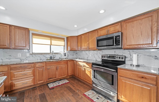 kitchen with appliances with stainless steel finishes, light stone countertops, dark wood-type flooring, decorative backsplash, and sink