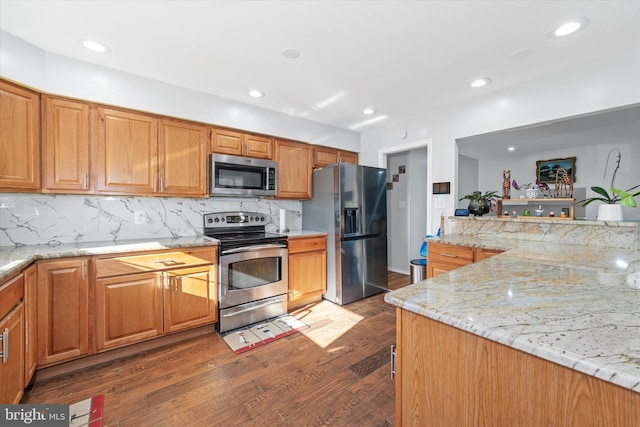 kitchen with appliances with stainless steel finishes, dark wood-type flooring, light stone counters, and backsplash