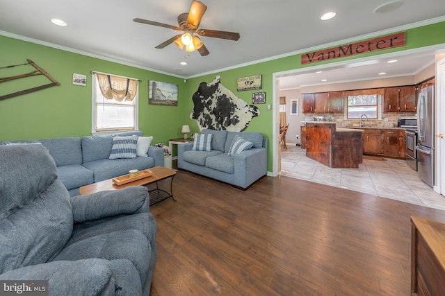 living room featuring ceiling fan, light wood-type flooring, ornamental molding, and sink