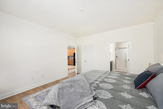 bedroom featuring black fridge, ensuite bathroom, and hardwood / wood-style flooring