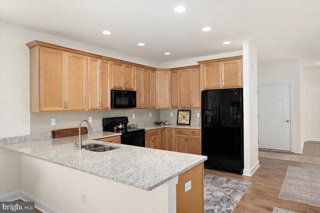 kitchen featuring kitchen peninsula, light wood-type flooring, light stone counters, sink, and black appliances