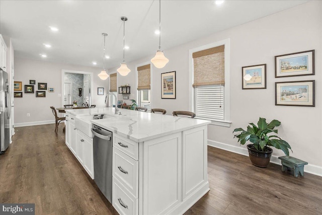 kitchen with stainless steel appliances, light stone counters, an island with sink, decorative light fixtures, and white cabinets