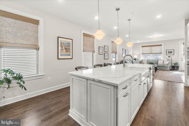 kitchen featuring pendant lighting, white cabinets, sink, light stone countertops, and an island with sink