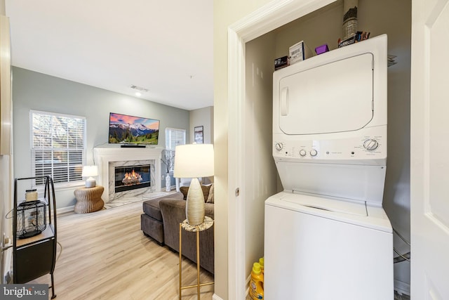 laundry area featuring stacked washer and dryer, a high end fireplace, and light hardwood / wood-style flooring