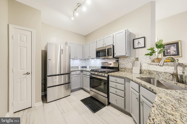 kitchen featuring gray cabinetry, light stone countertops, sink, stainless steel appliances, and decorative backsplash