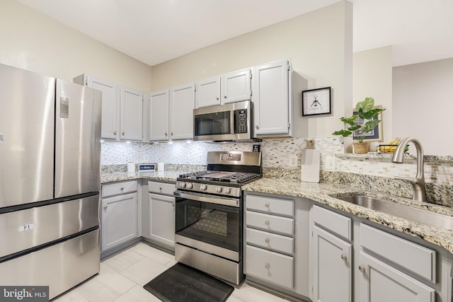 kitchen with light stone countertops, sink, backsplash, light tile patterned flooring, and appliances with stainless steel finishes