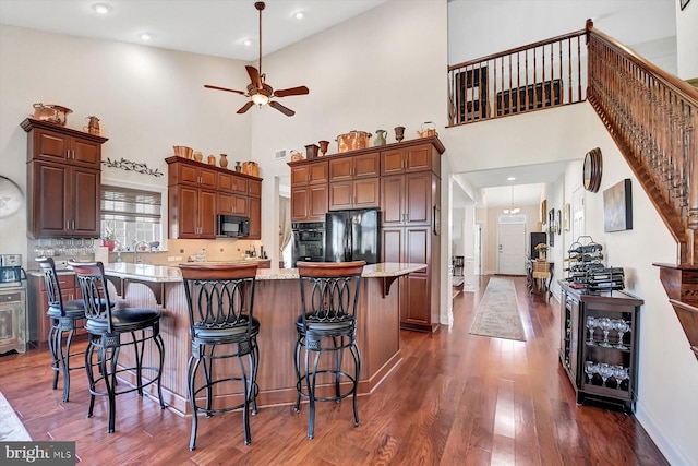 kitchen featuring dark wood-type flooring, a breakfast bar, a center island, light stone countertops, and black appliances