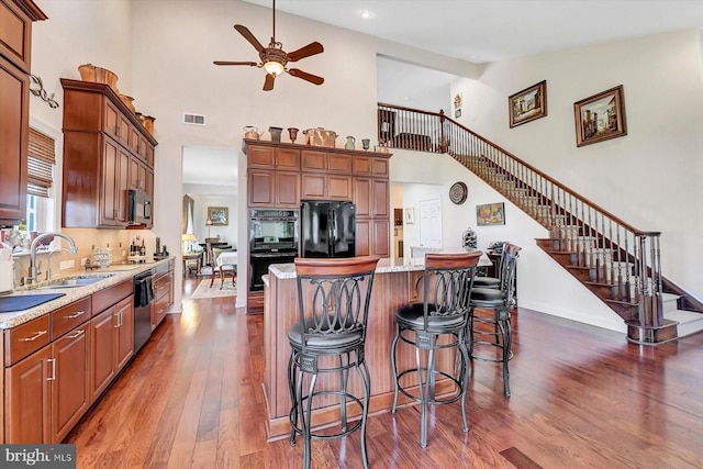 kitchen featuring sink, a center island, light stone counters, black appliances, and dark wood-type flooring