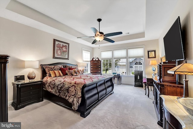 carpeted bedroom with a raised ceiling and ceiling fan