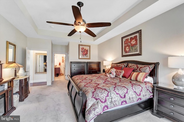 bedroom with connected bathroom, light colored carpet, a raised ceiling, and ceiling fan