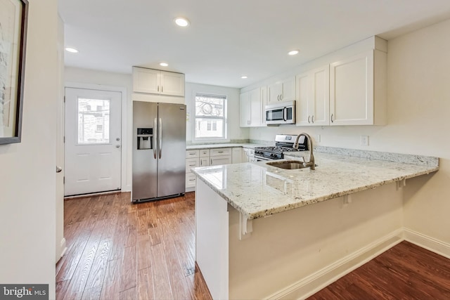 kitchen featuring kitchen peninsula, stainless steel appliances, sink, light hardwood / wood-style flooring, and white cabinetry