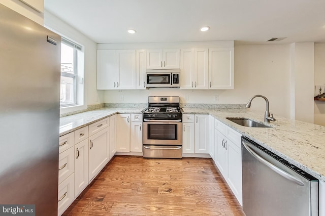 kitchen with kitchen peninsula, appliances with stainless steel finishes, white cabinetry, and sink