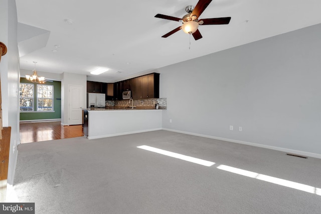 unfurnished living room featuring ceiling fan with notable chandelier, light colored carpet, and sink