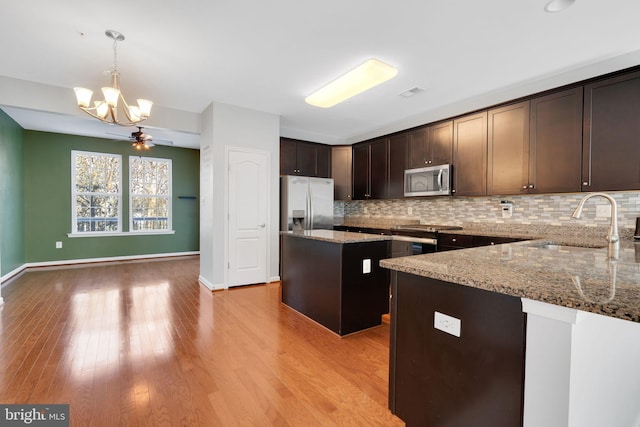 kitchen featuring pendant lighting, a center island, sink, light stone countertops, and appliances with stainless steel finishes