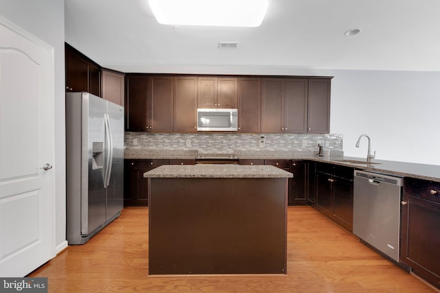 kitchen featuring appliances with stainless steel finishes, a kitchen island, light hardwood / wood-style flooring, light stone counters, and sink