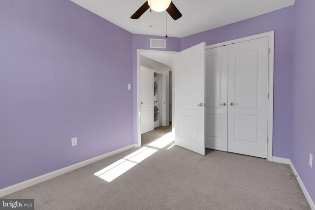 unfurnished bedroom featuring ceiling fan, stacked washer / dryer, a closet, and light carpet