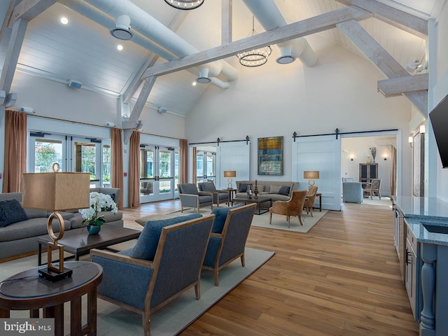 living room with french doors, beam ceiling, a barn door, high vaulted ceiling, and light hardwood / wood-style floors