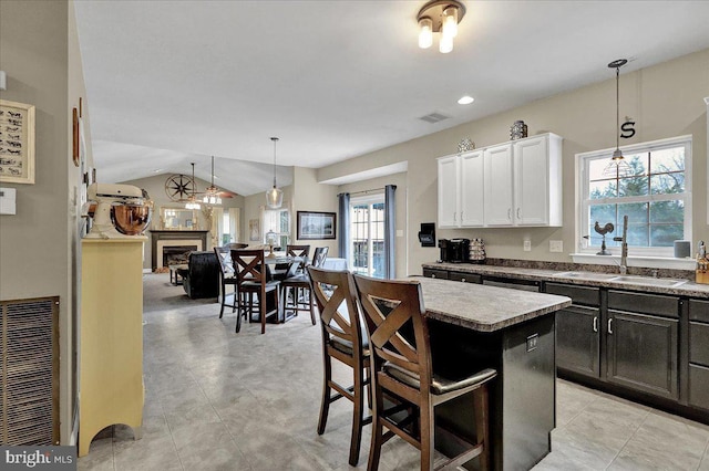 kitchen with lofted ceiling, white cabinets, hanging light fixtures, a kitchen island, and a kitchen bar