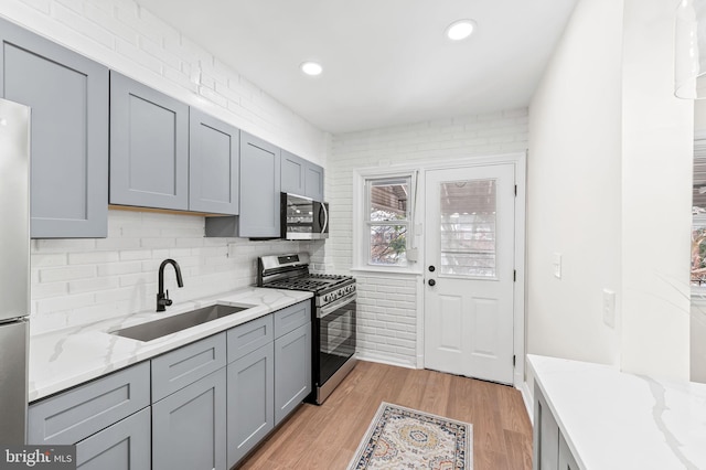 kitchen with sink, gray cabinets, light stone countertops, light wood-type flooring, and stainless steel appliances