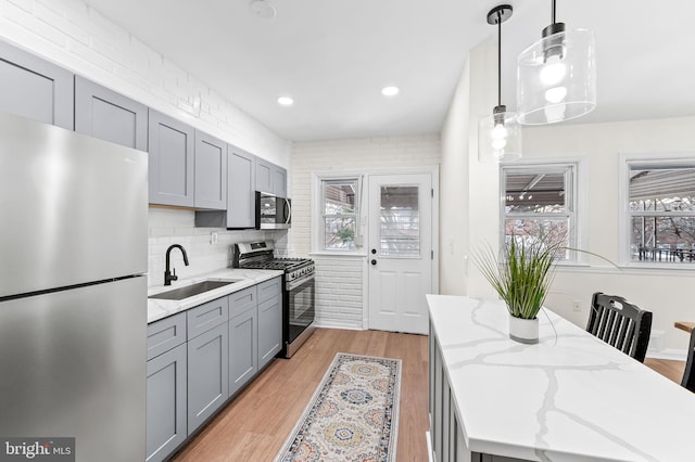 kitchen with light stone counters, stainless steel appliances, sink, pendant lighting, and gray cabinets