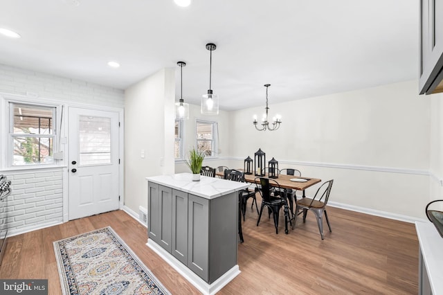 kitchen with gray cabinetry, light stone countertops, a wealth of natural light, hanging light fixtures, and light hardwood / wood-style floors