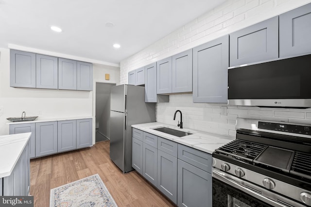 kitchen featuring stainless steel appliances, light hardwood / wood-style floors, gray cabinetry, and sink