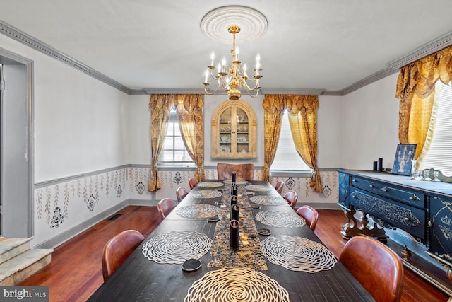 dining space with wood-type flooring, ornamental molding, and a notable chandelier