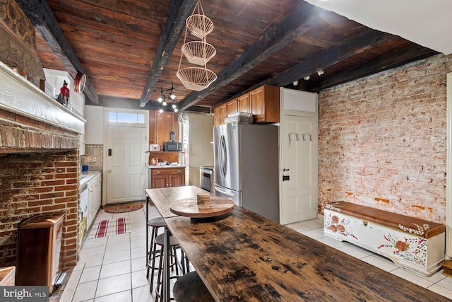 kitchen featuring appliances with stainless steel finishes, light tile patterned floors, wood ceiling, and beam ceiling