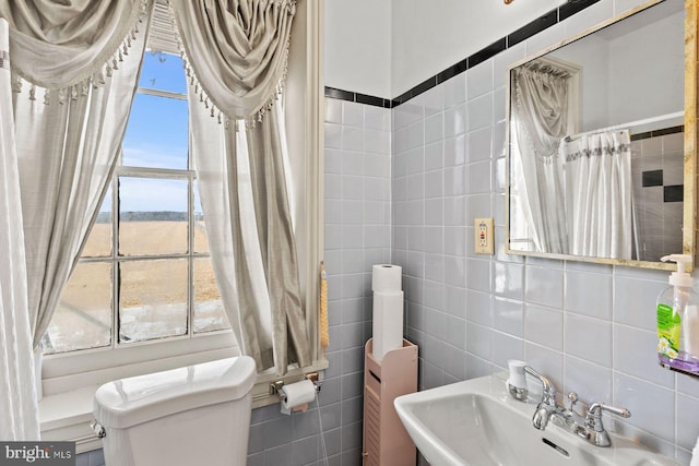 bathroom with toilet, sink, and tile walls