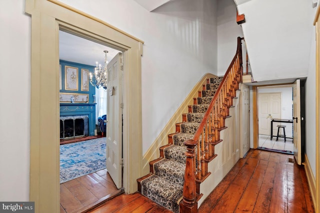 staircase with hardwood / wood-style floors, a notable chandelier, and a premium fireplace