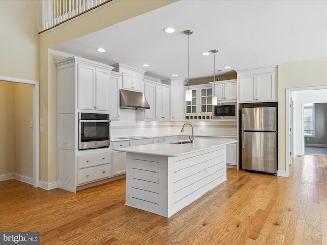 kitchen featuring sink, light hardwood / wood-style floors, decorative light fixtures, a kitchen island with sink, and appliances with stainless steel finishes