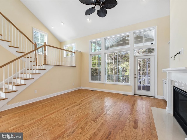 unfurnished living room with ceiling fan, light wood-type flooring, a high end fireplace, and a towering ceiling