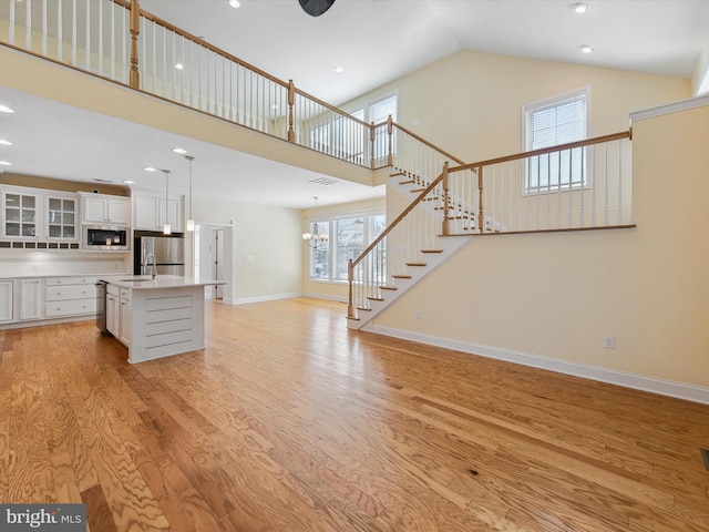 unfurnished living room with light hardwood / wood-style floors, sink, and high vaulted ceiling