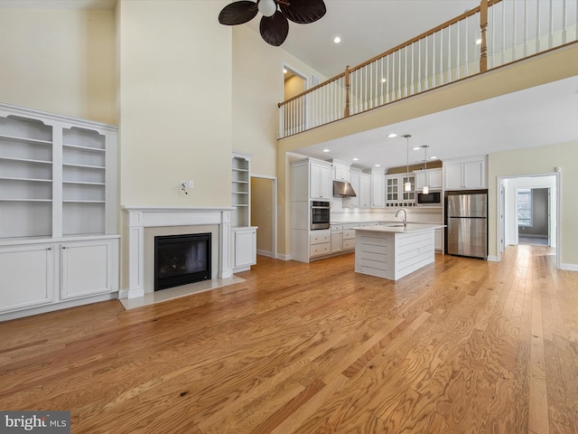 unfurnished living room with ceiling fan, light wood-type flooring, a towering ceiling, and sink