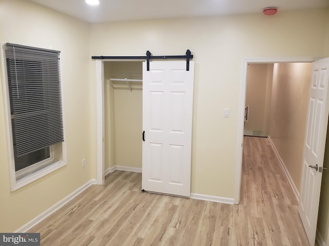 unfurnished bedroom with a barn door, a closet, and light hardwood / wood-style flooring